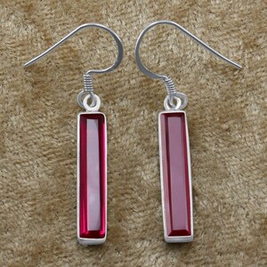 May include: A pair of silver dangle earrings with rectangular red gemstone drops.
