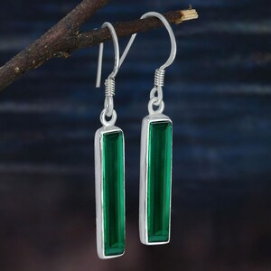 May include: A pair of silver dangle earrings with green rectangular gemstones. The earrings have a simple design and are perfect for everyday wear.