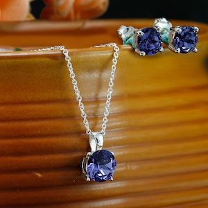 Puede incluir: Un conjunto de collar y pendientes de plata con un colgante redondo de piedra preciosa de color p&uacute;rpura oscuro y pendientes a juego.