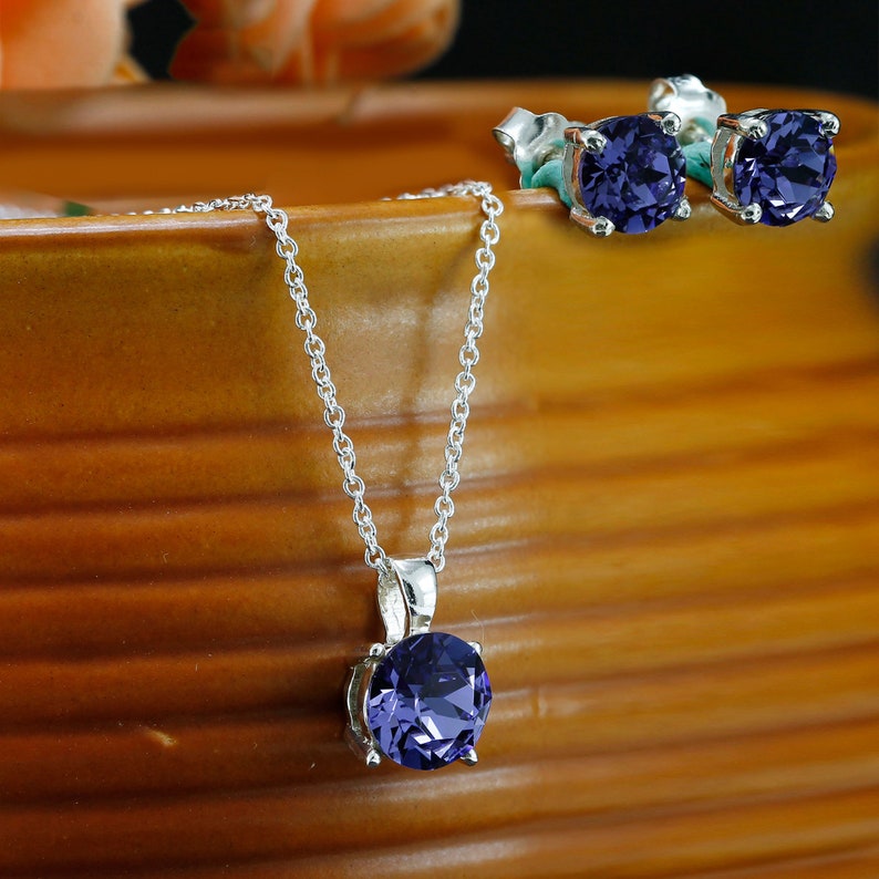 Puede incluir: Un conjunto de collar y pendientes de plata con un colgante redondo de piedra preciosa de color p&uacute;rpura oscuro y pendientes a juego.