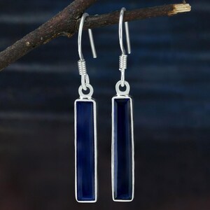 May include: A pair of silver dangle earrings with dark blue rectangular gemstones.