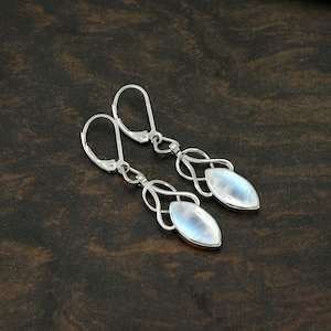 Può includere: Un paio di orecchini d'argento con una pietra di luna a forma di lacrima. Gli orecchini hanno un design delicato e intricato.