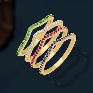 May include: Four gold rings with a wavy design. The rings are set with small gemstones in different colors: green, white, red, and blue.
