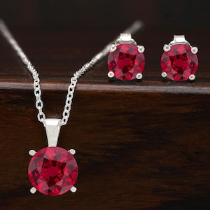 Peut inclure: Un ensemble de collier et boucles d'oreilles en argent avec une grande pierre précieuse rouge ronde. Le collier a une chaîne délicate et les boucles d'oreilles sont de style clou.