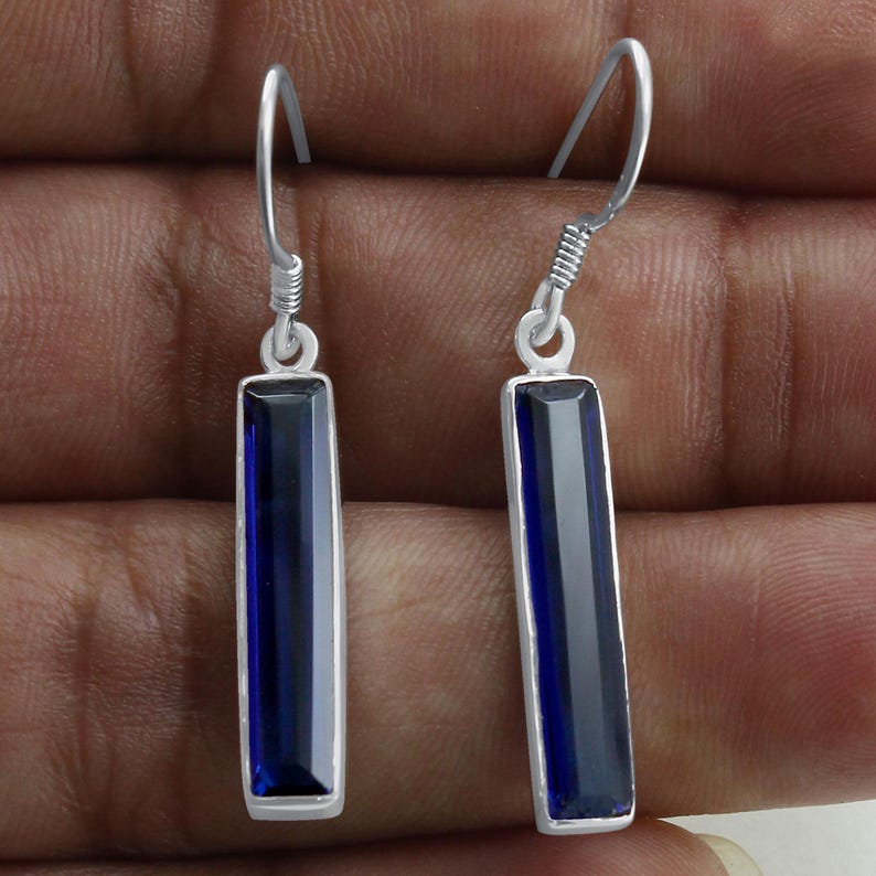 May include: A pair of silver dangle earrings with dark blue rectangular gemstones. The earrings have a simple design and are perfect for everyday wear.