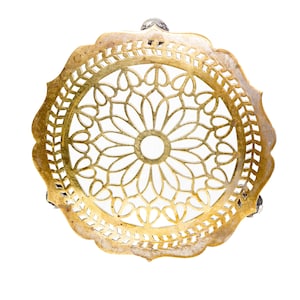 May include: A gold metal decorative stand with a round top and three legs. The top features a delicate, intricate design of cut-out circles and floral patterns.