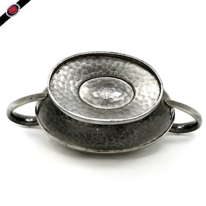 May include: A silver-toned, hammered metal sugar bowl with two handles. The bowl has an oval base and a textured surface. The underside of the bowl features stamped text, including "A.E. POSTON & CO. LONDON ENGLISH PRO 243".