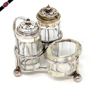 Könnte beinhalten: Ein Vintage-Gewürzset aus versilbertem Metall mit drei transparenten Glasbehältern. Das Set umfasst einen Salzstreuer, einen Pfefferstreuer und eine kleine offene Schale, die alle in einem dekorativen Metallrahmen gehalten werden. Die Salz- und Pfefferstreuer haben perforierte Deckel.