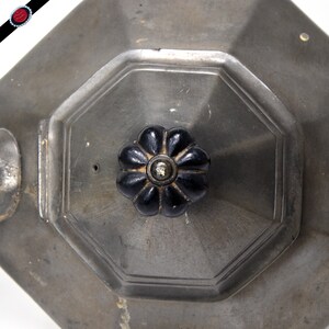 May include: A silver teapot with a black, flower-shaped knob on the lid. The teapot has an octagonal shape and a spout on the side.