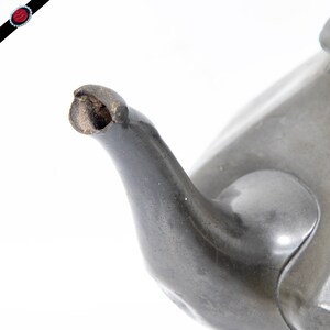 May include: Close-up of the spout of a pewter teapot. The spout is slightly chipped and shows signs of wear.
