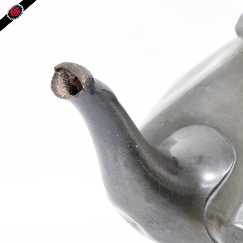 May include: Close-up of the spout of a pewter teapot. The spout is slightly chipped and shows signs of wear.