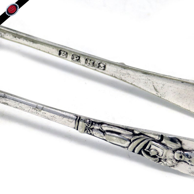 May include: A pair of silver sugar tongs with an ornate design on the handles. The tongs are marked with the inscription "B.R. 1913".