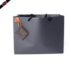 May include: A black gift bag with black handles and a red wax seal. A black tag with the text "Time to be Beautiful" is attached to the bag.