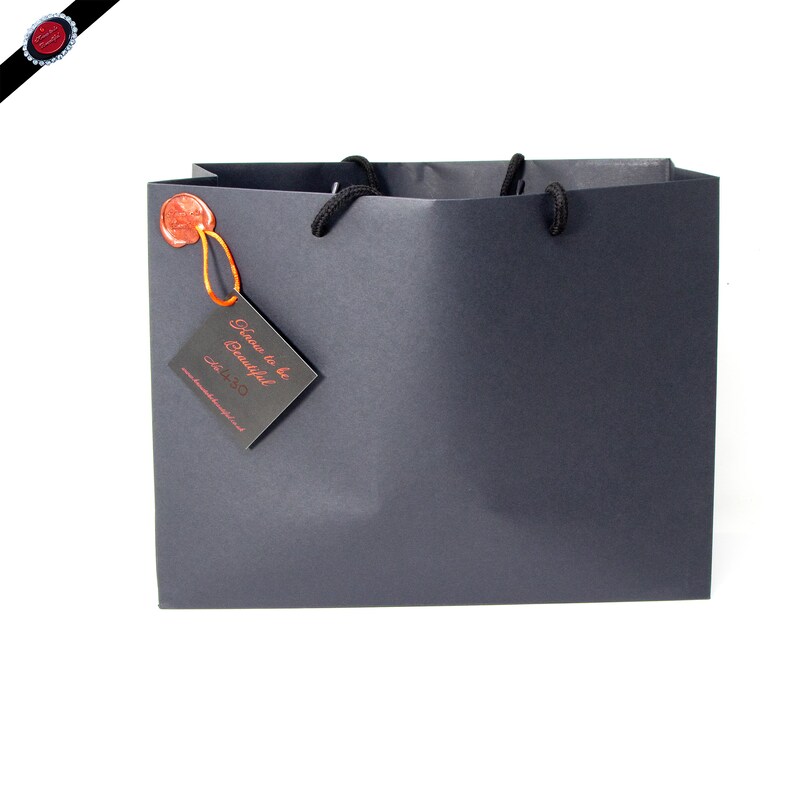 May include: A black gift bag with black handles and a red wax seal. A black tag with the text "Time to be Beautiful" is attached to the bag.
