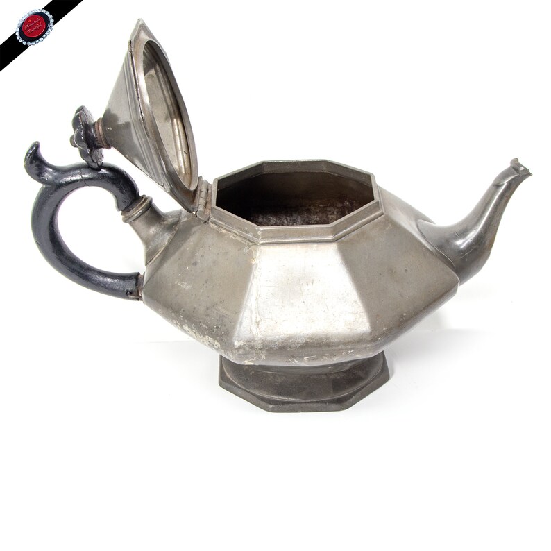 May include: A silver teapot with a black handle and a lid that is open. The teapot has an octagonal shape and a base.