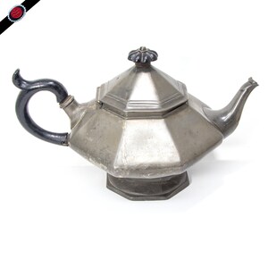 A stunning large pewter teapot, in an octagonal shape with heavily sloping sides and a pedestal.  The handle and finial are carved wood, painted black.  Made by Broadhead and Atkin in the mid 1800s