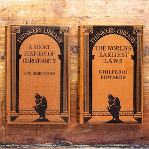 May include: Two orange hardback books from the Thinkers Library series. The left book is titled A Short History of Christianity by J.M. Robertson. The right book is titled The World's Earliest Laws by Chilperic Edwards. Both feature black illustrations.