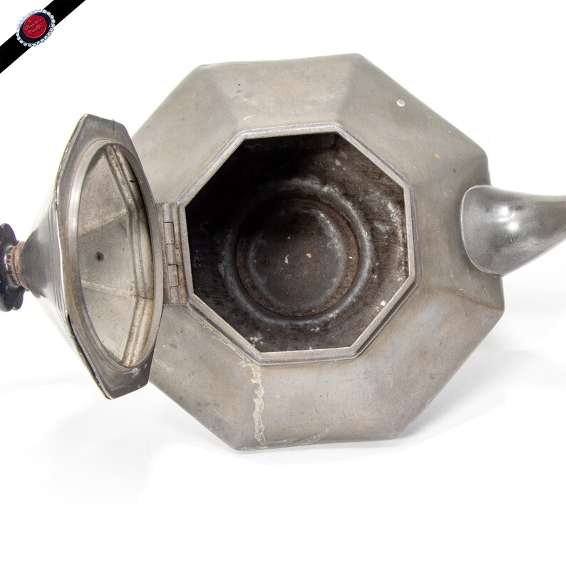 May include: A silver octagonal teapot with a hinged lid. The teapot is open and the inside is visible.