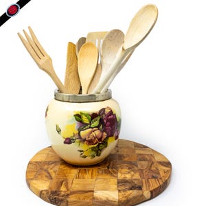 Może przedstawiać: Zestaw drewnianych przyborów kuchennych, w tym łyżki i widelec, jest prezentowany w ceramicznym słoiku z kwiatowym wzorem. Słoik stoi na okrągłej, drewnianej desce do krojenia.