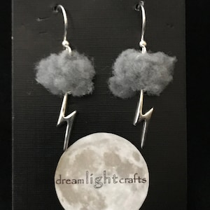 May include: Silver earrings featuring grey felt clouds and lightning bolt charms. The earrings are shown against a black background with a moon and the text "dreamlightcrafts".