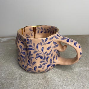 Puede incluir: Un juego de tres tazas de cerámica con acabado mate moteado. Las tazas son de color crema, marrón claro y marrón oscuro. Cada taza tiene un diseño simple y minimalista.