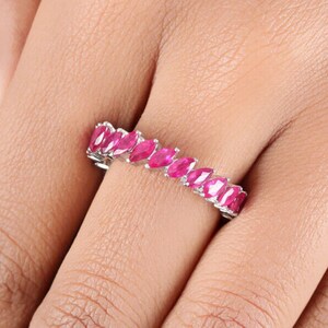 Può includere: Un anello a fascia d'argento con una fila di pietre preziose rosa a forma di marquise.