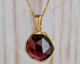 May include: A gold chain necklace with a pendant featuring a large, faceted, dark red gemstone set in a gold bezel.