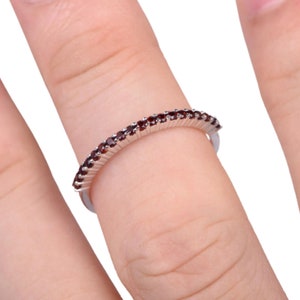 Può includere: Un anello a fascia d'argento con una fila di piccole pietre preziose rosso scuro.