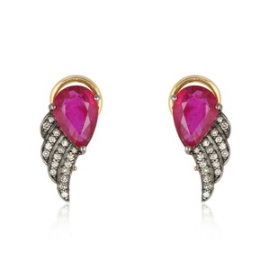 May include: A pair of earrings with a pink gemstone and a silver wing design. The wings are encrusted with small clear stones.