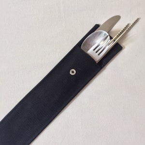 May include: A black fabric utensil case with a silver snap closure, containing a stainless steel knife, spoon, fork, and chopsticks. The utensils are neatly arranged inside the case, ready for use.