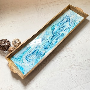 May include: A wooden serving tray with a blue and white marbled resin inlay. The tray has a rectangular shape and rounded edges.