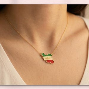 May include: A gold necklace with a pendant shaped like a country, with green, white, and red enamel. The necklace is around the neck. The text "SENASTIONAL JEWEL" is at the top, and "STERLING SILVER | 14K SOLID GOLD" is at the bottom.