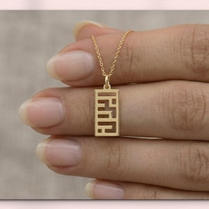 Op de afbeelding: Een goudkleurige hangerketting met een rechthoekig ontwerp. De ketting wordt door een hand vastgehouden. De tekst "SENASTIONAL JEWEL" staat bovenaan de afbeelding. De tekst "STERLING SILVER | 14K SOLID GOLD" staat onderaan.