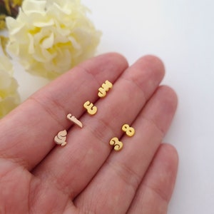 May include: A set of gold-colored earrings featuring the numbers 3, 5, and 8. The earrings are small and delicate, and they would make a great gift for a friend or loved one.