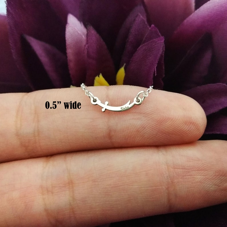 May include: A silver necklace with a crescent moon pendant and a small cross. The pendant is 0.5 inches wide and has the word "Sinn" engraved on it.