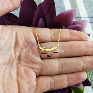May include: Gold necklace with a curved pendant featuring Arabic calligraphy. The pendant measures 0.8 inches in length.
