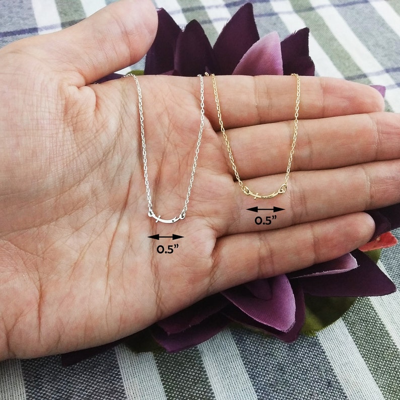 May include: Two delicate necklaces with a simple curved design, one silver and one gold, each measuring 0.5 inches in length. The necklaces are displayed on a hand.