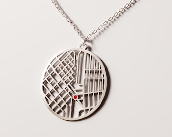 May include: Silver-colored pendant necklace featuring a circular map design. The map has a grid pattern with a small red dot. The pendant hangs from a delicate chain, creating a minimalist and modern aesthetic.