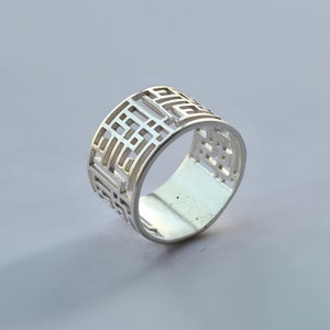 Peut inclure: Une bague en argent avec un motif géométrique. La bague est en métal avec une finition brillante.