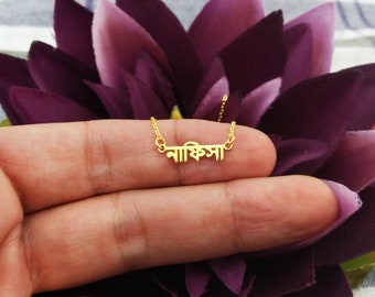 May include: A gold necklace with the Bengali word "নাক্ষত্র" (meaning "star") hanging on a finger.