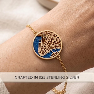May include: A gold-toned bracelet featuring a circular pendant with a detailed street map cutout design. The pendant includes a deep blue enamel inlay representing water. The text CRAFTED IN 925 STERLING SILVER is printed at the bottom.