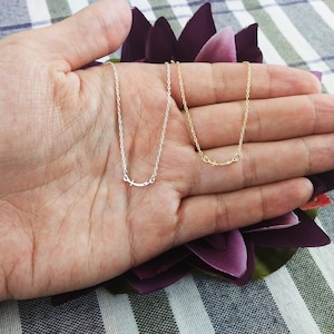 May include: Two delicate necklaces with a simple curved design, one in silver and one in gold, displayed on a hand.