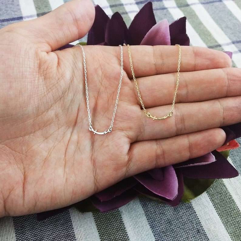 May include: Two delicate necklaces with a simple curved design, one in silver and one in gold, displayed on a hand.