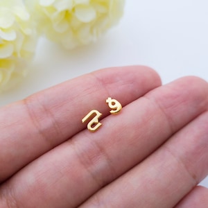 May include: A pair of gold initial earrings, one with the letter "N" and the other with the letter "g".