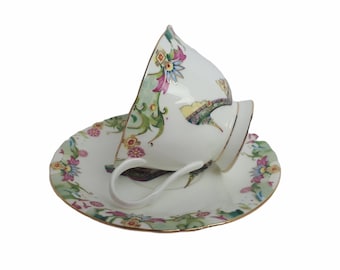 May include: A white teacup and saucer set with a floral design in shades of pink, green, and blue. The cup and saucer have a gold trim.