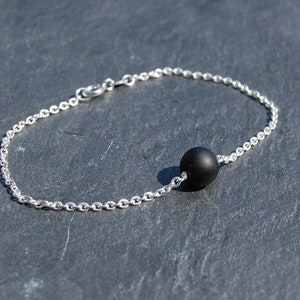 Op de afbeelding: Een zilveren kettingarmband met een enkele zwarte kraal.