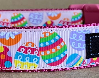 Puede incluir: Un collar rosa para perros con un patrón repetido de coloridos huevos de Pascua. El collar tiene una hebilla de plástico rosa y una anilla en D de metal. El nombre de la marca "WagTailCollars" se muestra en una etiqueta negra.