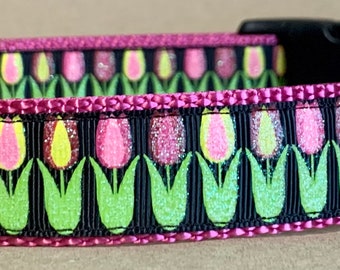 May include: A pink dog collar with a black and green tulip print. The collar has a black buckle and a silver D-ring. The collar has a black tag with the text "WayToCollar" in white.