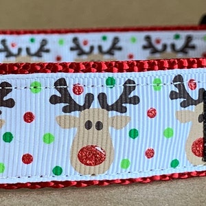 May include: Red and white dog collar with a reindeer pattern and red and green polka dots. The collar has a silver D-ring and a black tag that says "Wag Tail Collars".