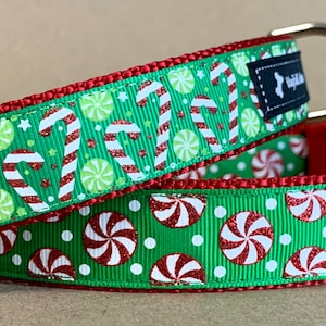 May include: Two green dog collars with a festive candy cane and peppermint pattern. The collars have red trim and feature candy canes, peppermints, and stars on a green background. Each collar has a black label with the text "WagTailColars".